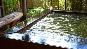 A wooden pool with clear water, surrounded by a bamboo fence and greenery.