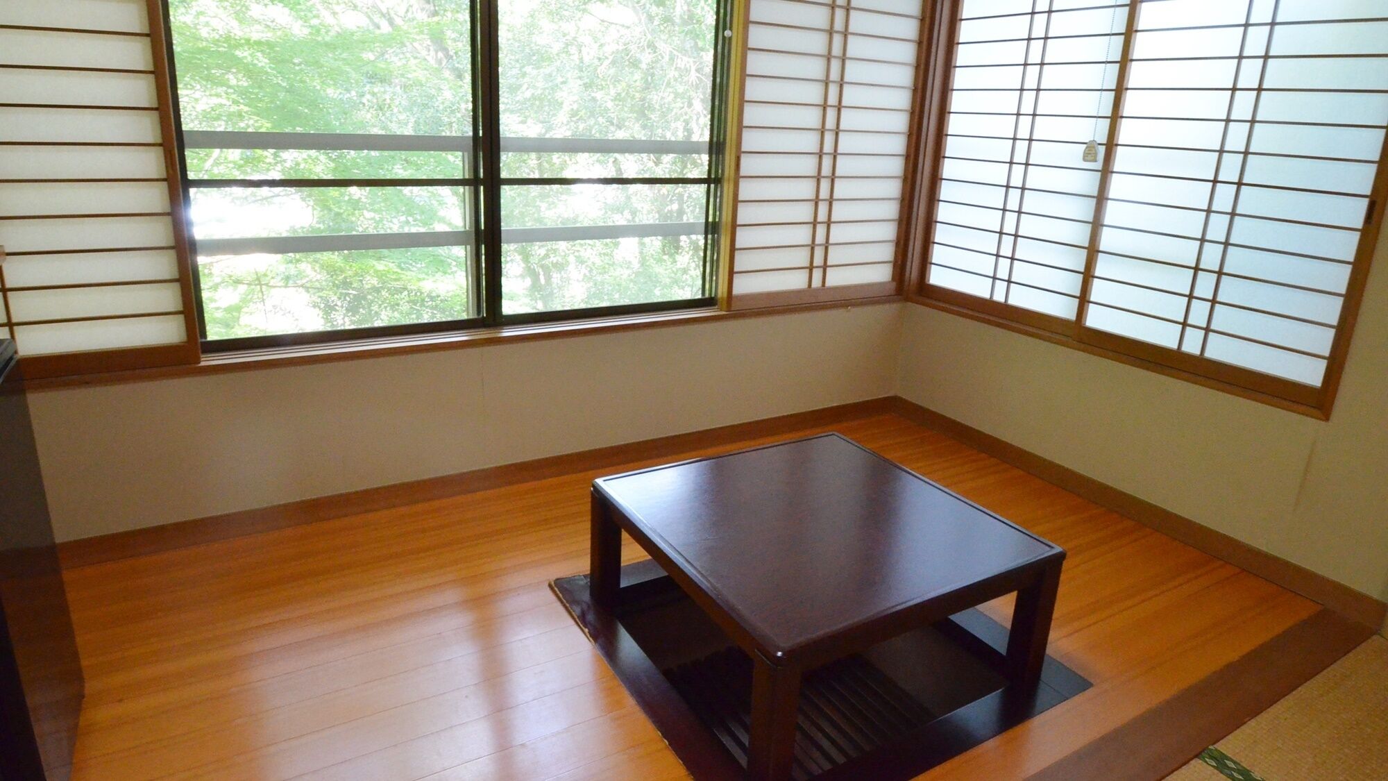 Una habitación con piso de madera, una mesa de madera oscura y puertas correderas japonesas que dan a vistas de árboles.