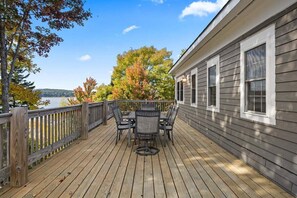 A wooden deck with a table and chairs, overlooking a body of water and trees.