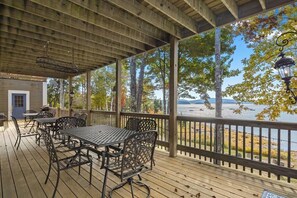 A covered outdoor deck with tables and chairs, overlooking a body of water and trees.