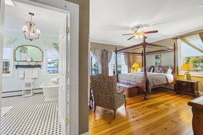 Een slaapkamer met een hemelbed, een kroonluchter, een plafondventilator en uitzicht op de omgeving.