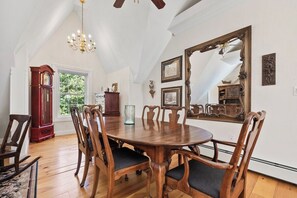 Een eetruimte met een houten tafel en stoelen, een kroonluchter, een grote spiegel en een staande klok.