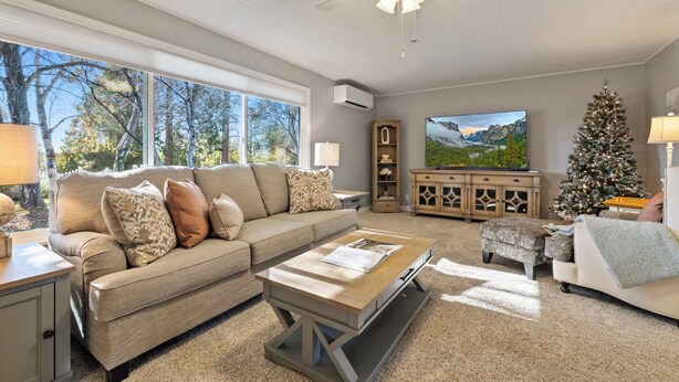 A spacious living room with a large window, a ceiling fan, a television, and a Christmas tree.