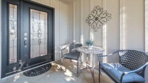 A front door with a glass panel, two chairs, a small table, and a decorative wall piece.