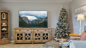 A living room with a large flat-screen TV, a wooden cabinet, a Christmas tree, and a cozy seating area.