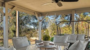 A covered patio with a glass table, white cushioned chairs, and a ceiling fan.