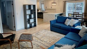 Un salon moderne avec un canapé bleu, un pouf à motifs et un lustre.
