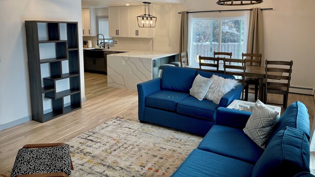Un salon moderne avec un canapé bleu, un tapis à motifs et un coin repas avec des chaises en bois.