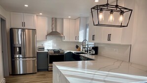 Une cuisine moderne dotée d’appareils électroménagers en acier inoxydable, d’un îlot en marbre et de luminaires suspendus.