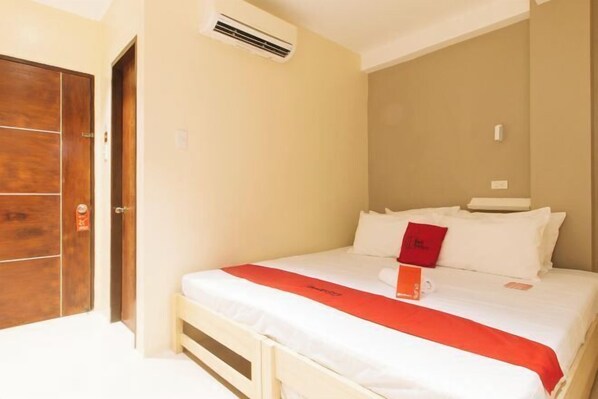 A hotel room with a bed, a wooden wardrobe, and an air conditioning unit.
