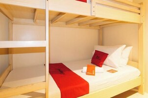 A bunk bed with a red blanket and pillows, a wooden headboard, and a small table with a book.