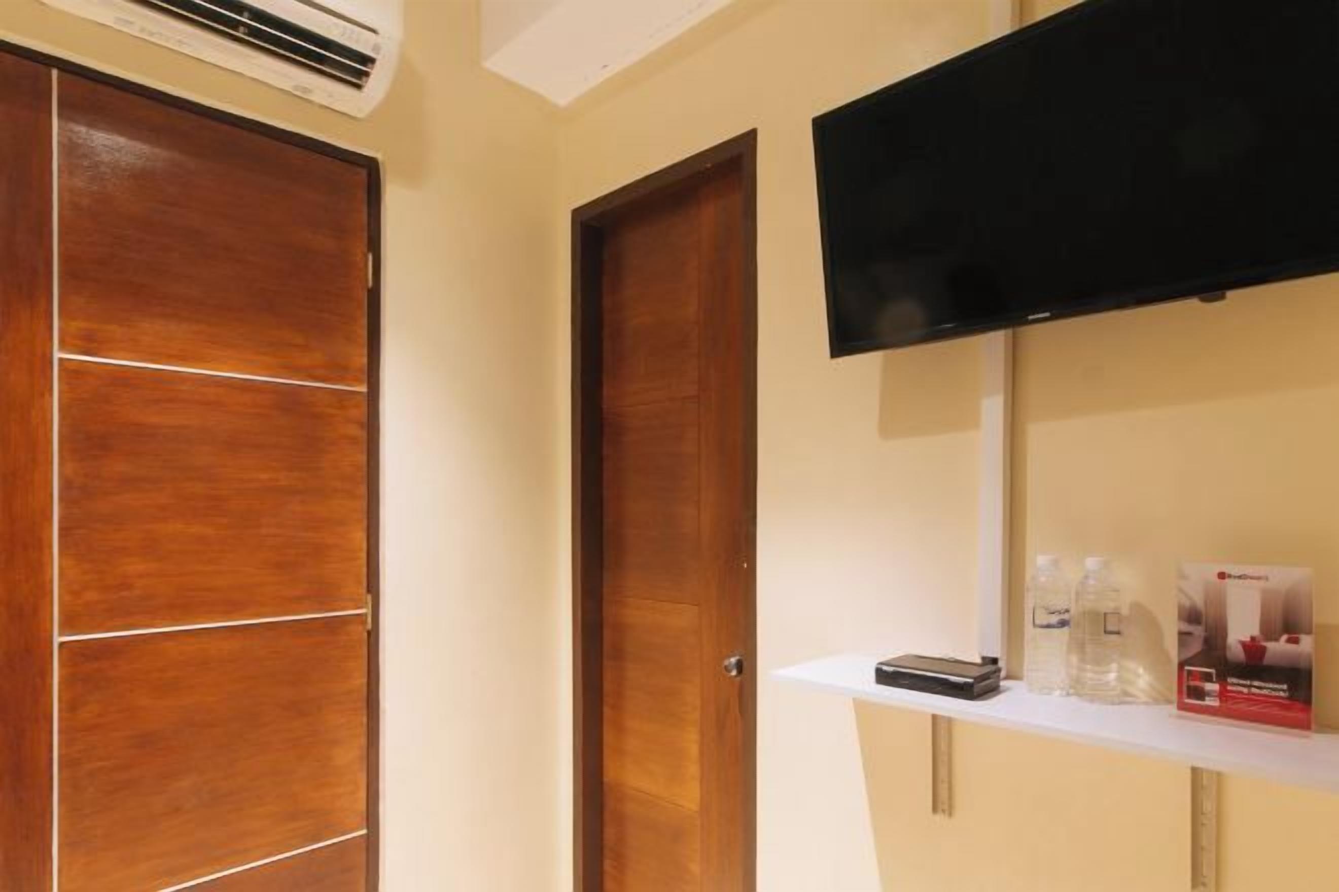 Habitación de hotel con un armario de madera, un televisor fijado a la pared y un estante con artículos de aseo.