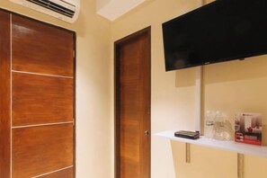 A hotel room with a wooden wardrobe, a television mounted on the wall, and a shelf with toiletries.