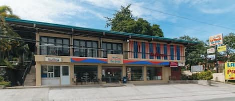 A two-story building with a flat roof, a storefront on the ground floor, and a signboard on the right side.