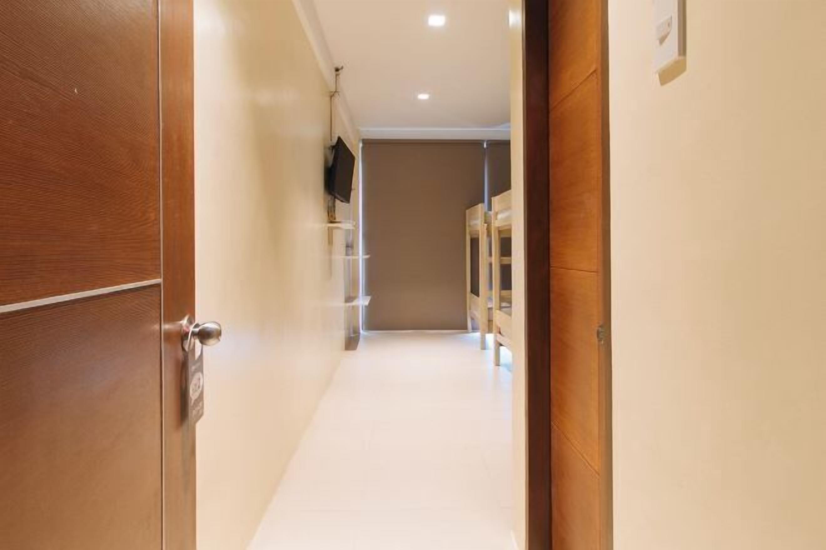 Un pasillo con una puerta de madera a la izquierda, una pared blanca y un televisor montado en la pared.