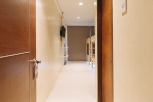 A hallway with a wooden door on the left, a white wall, and a television mounted on the wall.