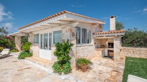 A stone house with a covered patio, a chimney, and potted plants.