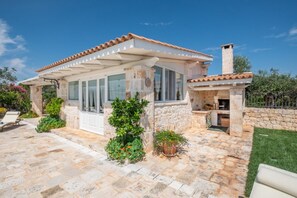 A stone house with a covered patio, a chimney, and potted plants.