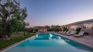 A swimming pool with lounge chairs, a stone building, and a tree.