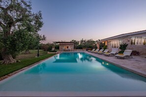 A swimming pool with lounge chairs, a stone building, and a tree.