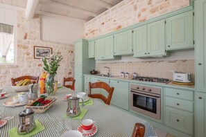 A kitchen with green cabinets, a stove, and a dining table set with plates and cups.