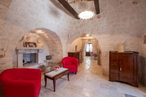 A stone-walled room with a fireplace, a red armchair, a wooden table, and a cabinet. - Villa Antica Dimora by MMega (Castellana Grotte)