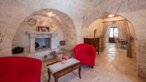A stone-walled room with a fireplace, a red armchair, and a table with a vase.