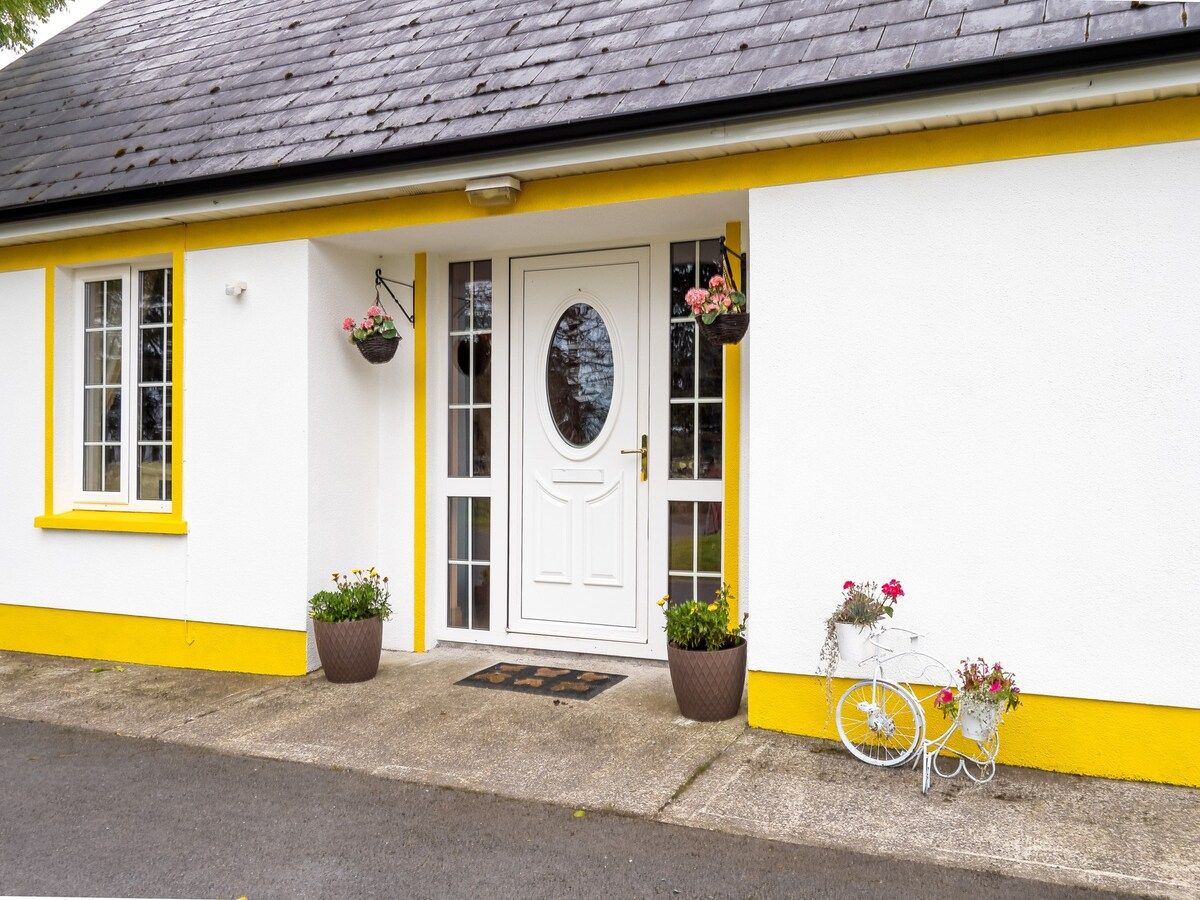 Una casa con puerta blanca, detalles en amarillo y una bicicleta con plantas en macetas a su lado.