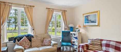 Un salon comprenant un canapé, un fauteuil et un divan à carreaux rouges et blancs. On y trouve également une bibliothèque remplie de livres et une lampe.