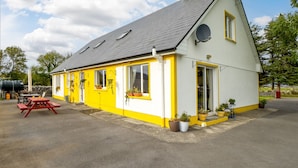 A yellow and white building with a grey roof, a satellite dish, and a red picnic table.