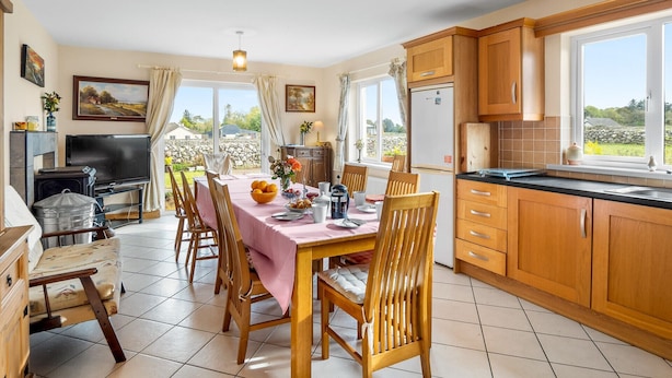 A dining area with a table set for four, wooden chairs, a pink tablecloth, and a bowl of fruit.