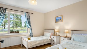 A bedroom with two single beds, a window with curtains, a radiator, and a painting on the wall.