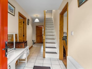 A hallway with a white staircase, wooden doors, and a white bench with drawers.