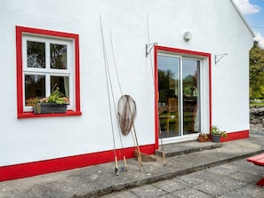 A white building with red trim, a window with a flower box, and fishing rods leaning against the wall.