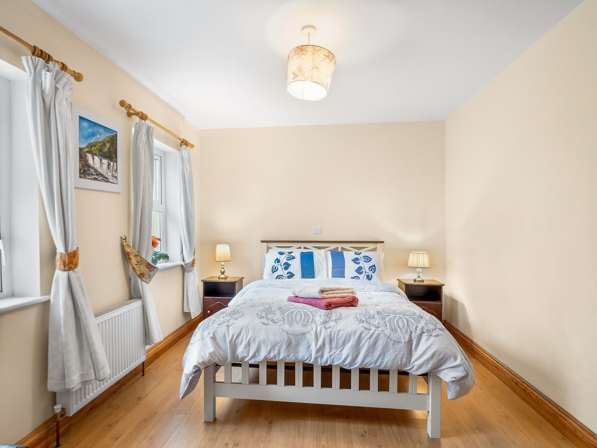 A bedroom with a bed, curtains, a nightstand, a lamp, and a picture on the wall.