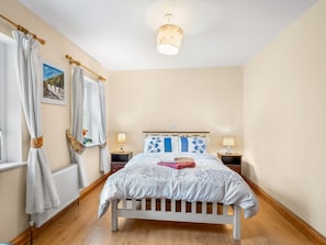 A bedroom with a bed, curtains, a nightstand, a lamp, and a picture on the wall.