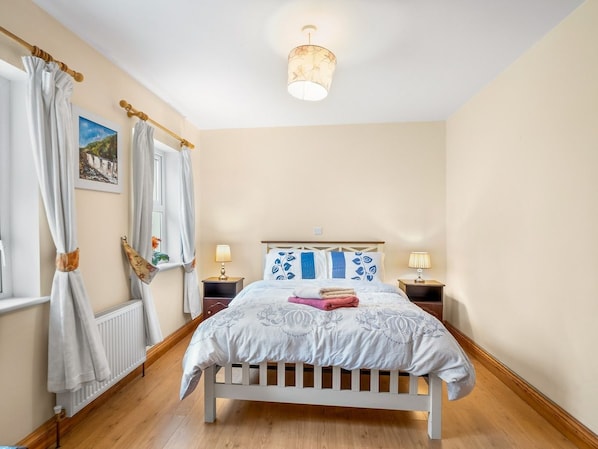 A bedroom with a bed, curtains, a nightstand, a lamp, and a picture on the wall.