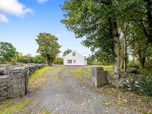 Situated at the end of a gravel driveway, this charming cottage is surrounded by lush greenery and stone walls.
