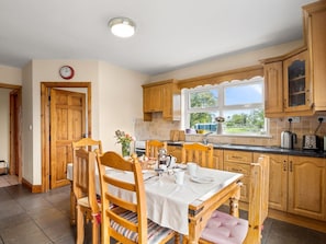 A kitchen with wooden cabinets, a dining table with chairs, a clock on the wall, and a window providing a view of the outdoors.