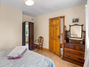 A bedroom with a bed, a wooden wardrobe, a chair, a dresser, and a door.