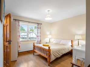 A bedroom with a wooden bed, a bedside table with a lamp, a window with curtains, and a radiator.