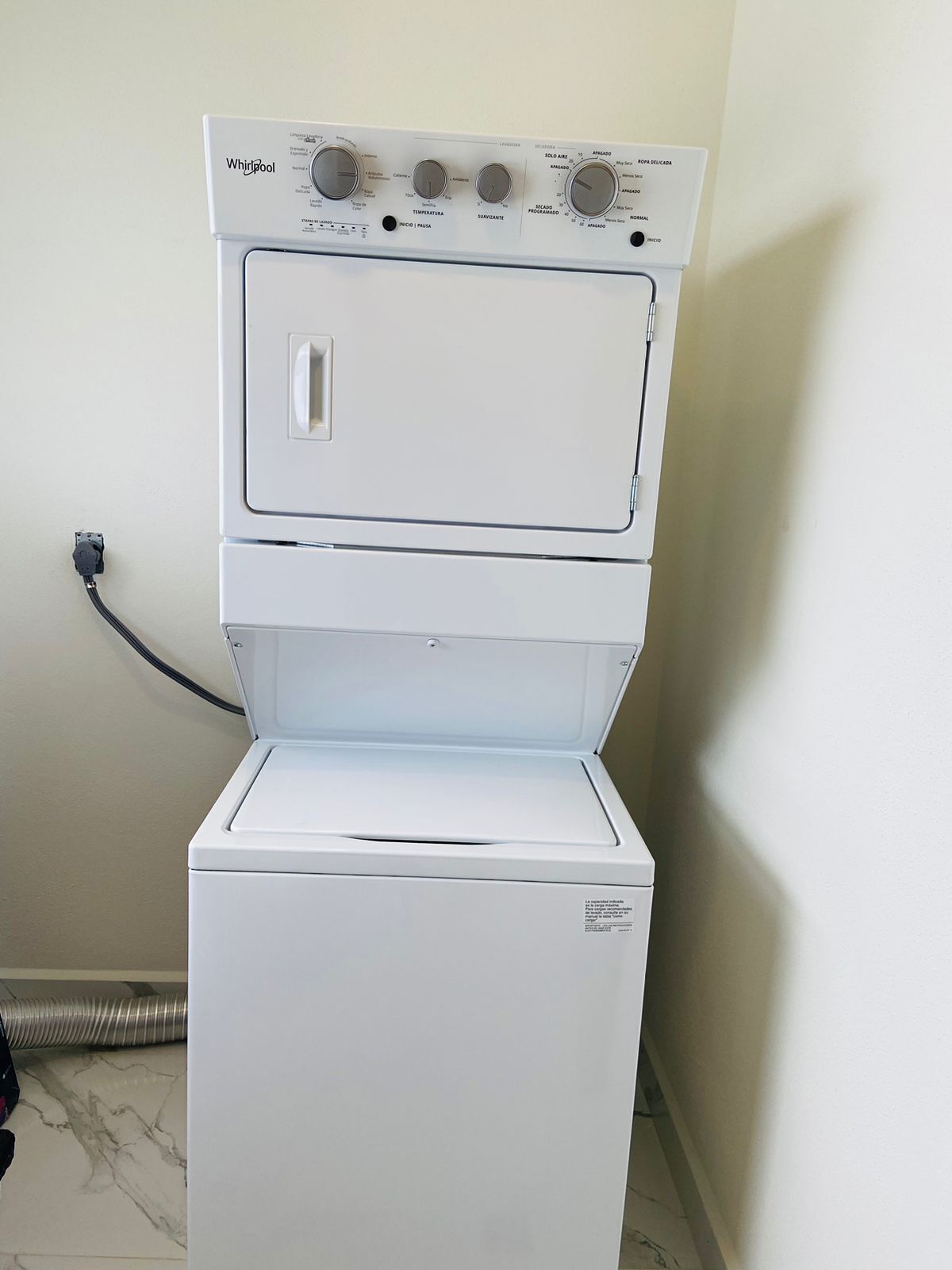 Un appareil combiné lave-linge et sèche-linge, de type « superposé », doté de boutons de commande et d’un câble d’alimentation branché.