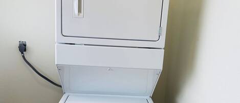 Un appareil combiné lave-linge et sèche-linge, de type « superposé », doté de boutons de commande et d’un câble d’alimentation branché.
