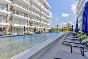 Un hotel moderno con piscina, tumbonas y sombrillas azules.