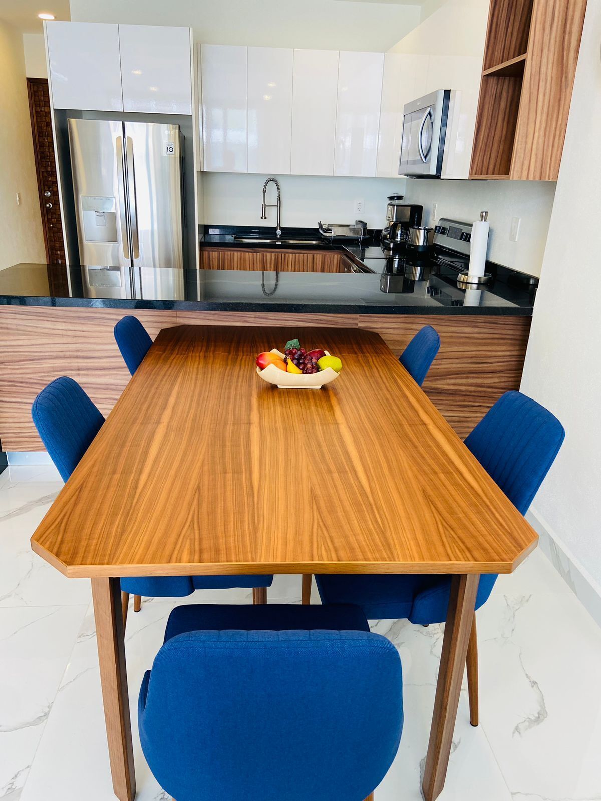 A modern kitchen with white cabinets, stainless steel appliances, and a wooden dining table with blue chairs.