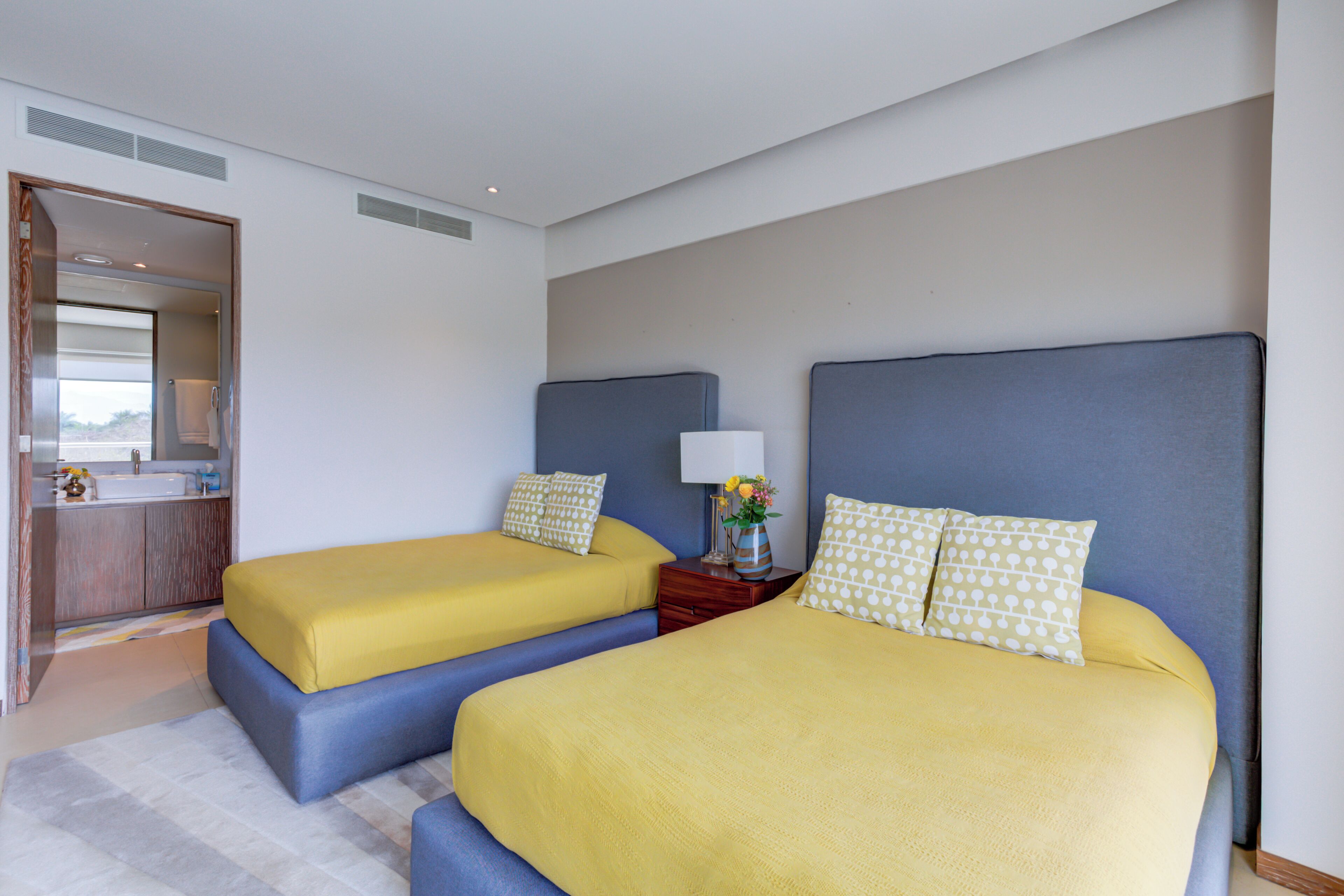 Habitación de hotel con dos camas, un baño y un pequeño escritorio con lámpara.