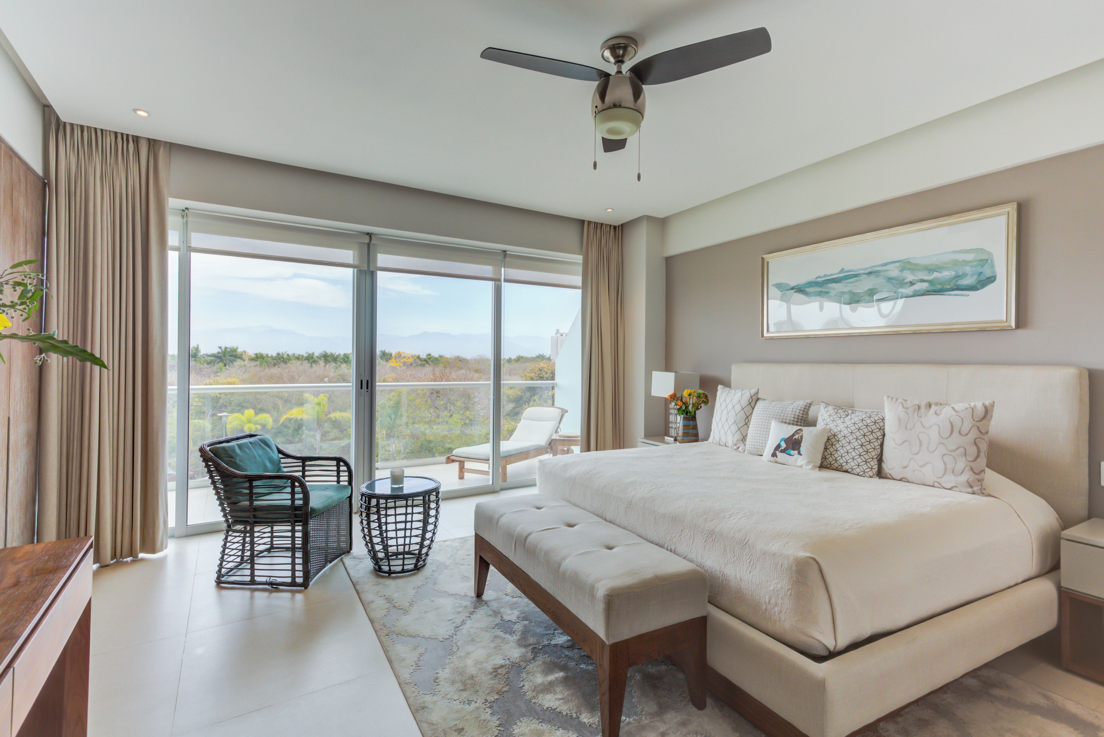 A spacious bedroom with a large bed, a ceiling fan, and a balcony with a chair.