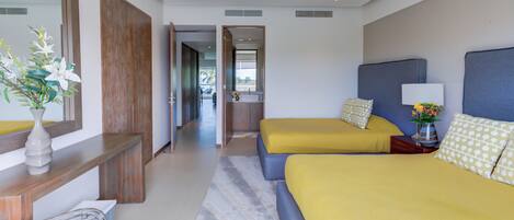 A hotel room with two beds, a large mirror, a bedside table with a vase of flowers, and a view of the hallway and bathroom.