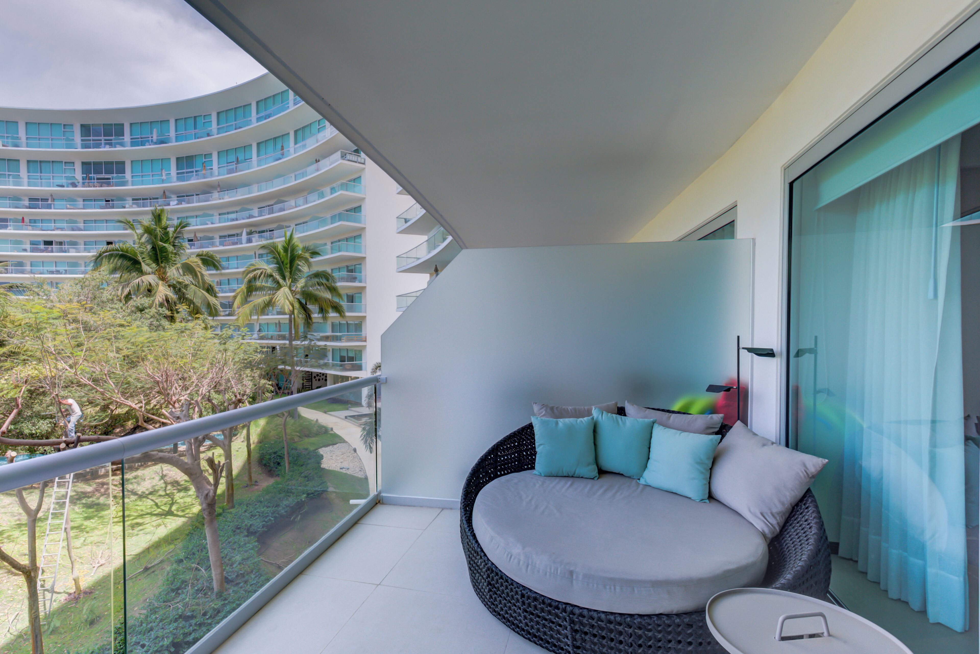 A balcony with a round seating area, a glass railing, and a view of a modern building and palm trees.