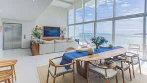 A modern living room with a large dining table, comfortable seating, a sofa, and a large window overlooking the sea. - Marítima Beachfront Playa Flamingos (Nuevo Nayarit)